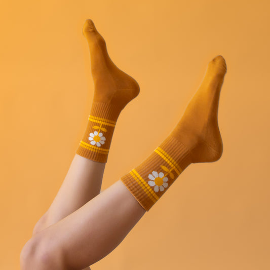 On a peachy background is a burnt orange pair of socks with a daisy graphic on the sides.
